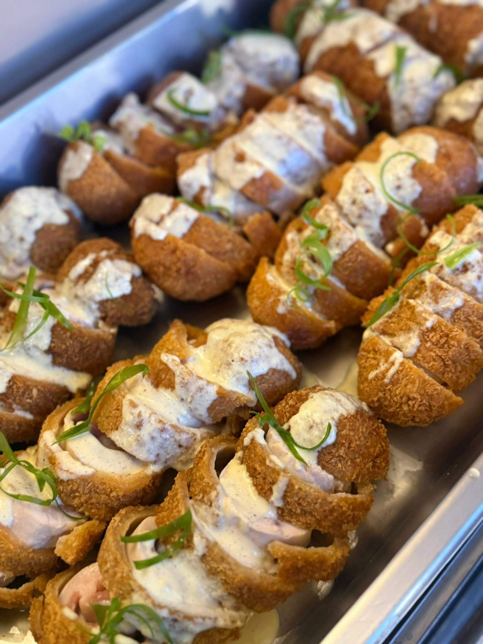 Golden breaded chicken rolls drizzled with cream sauce and spring onion