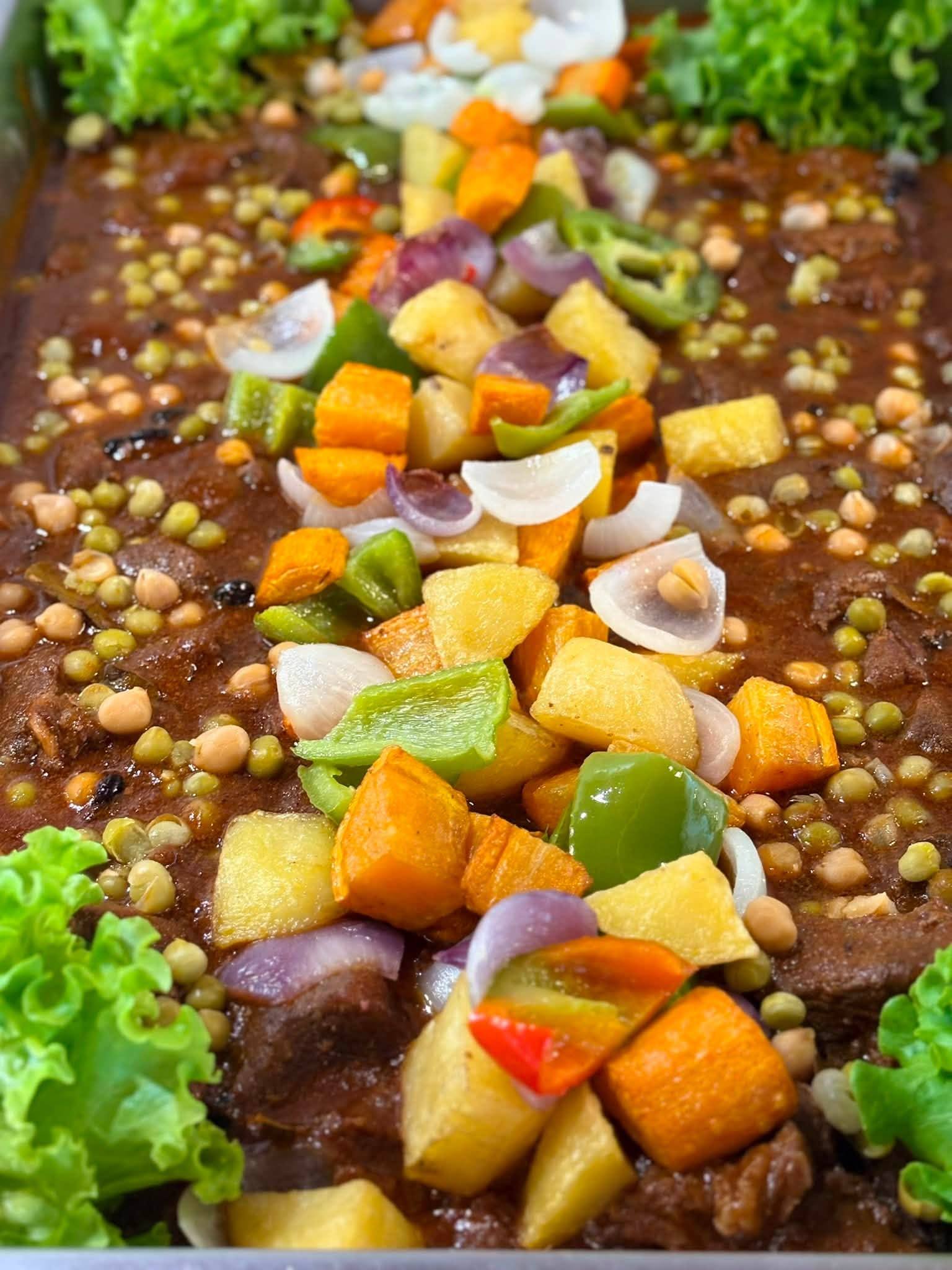 A rich tomato stew topped with potatoes, carrots, bell peppers, onions and peas
