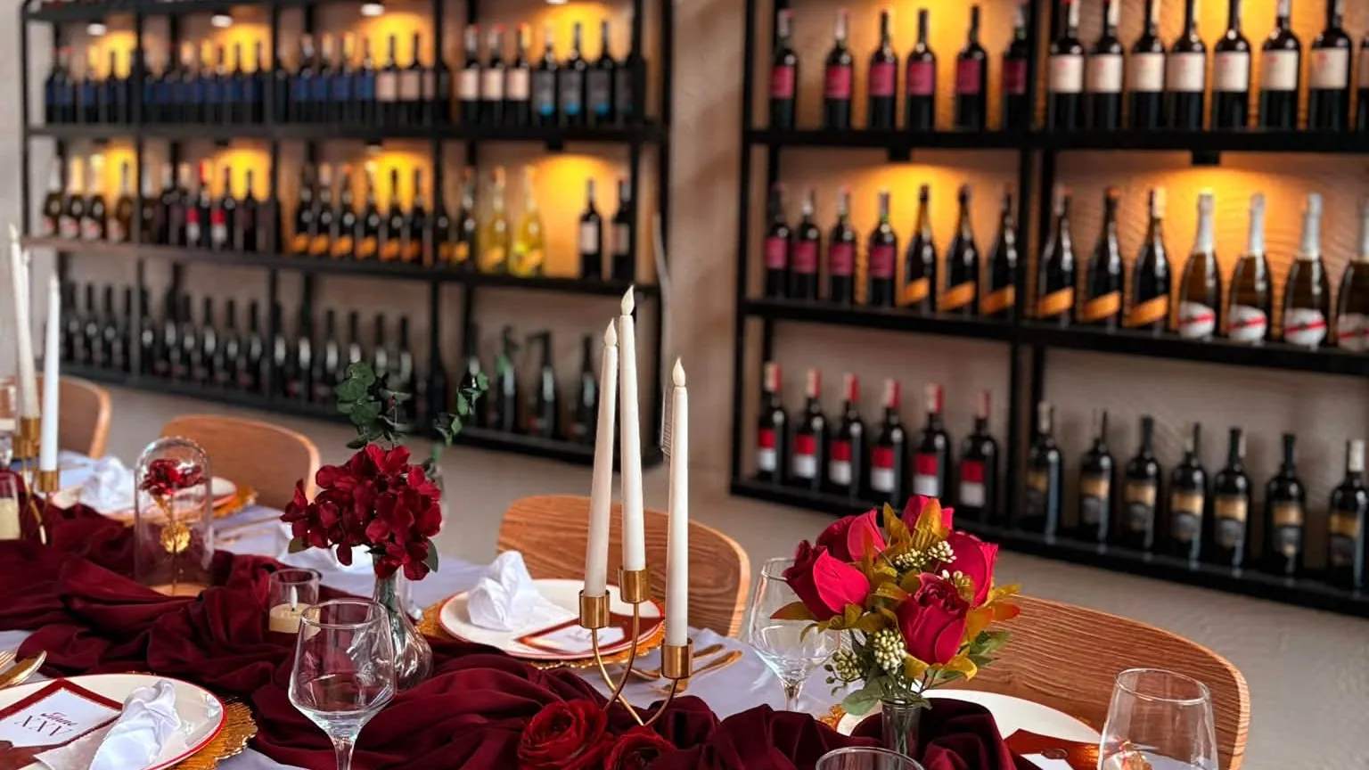 Candlelit table with red roses in front of La Bottega’s backlit wall of wine bottles