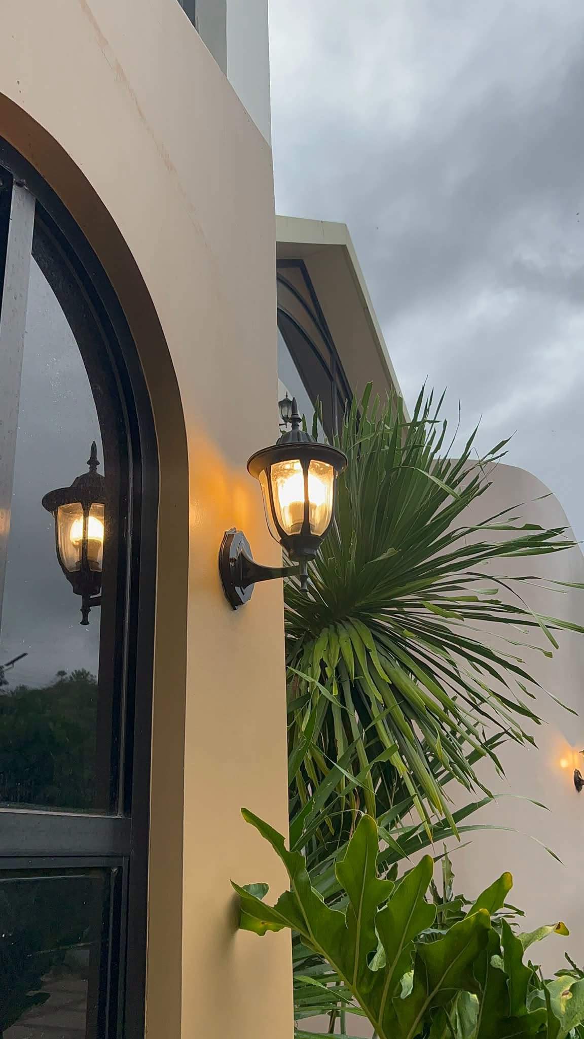 Arched window and lantern on the cream exterior wall, with a palm against a cloudy sky