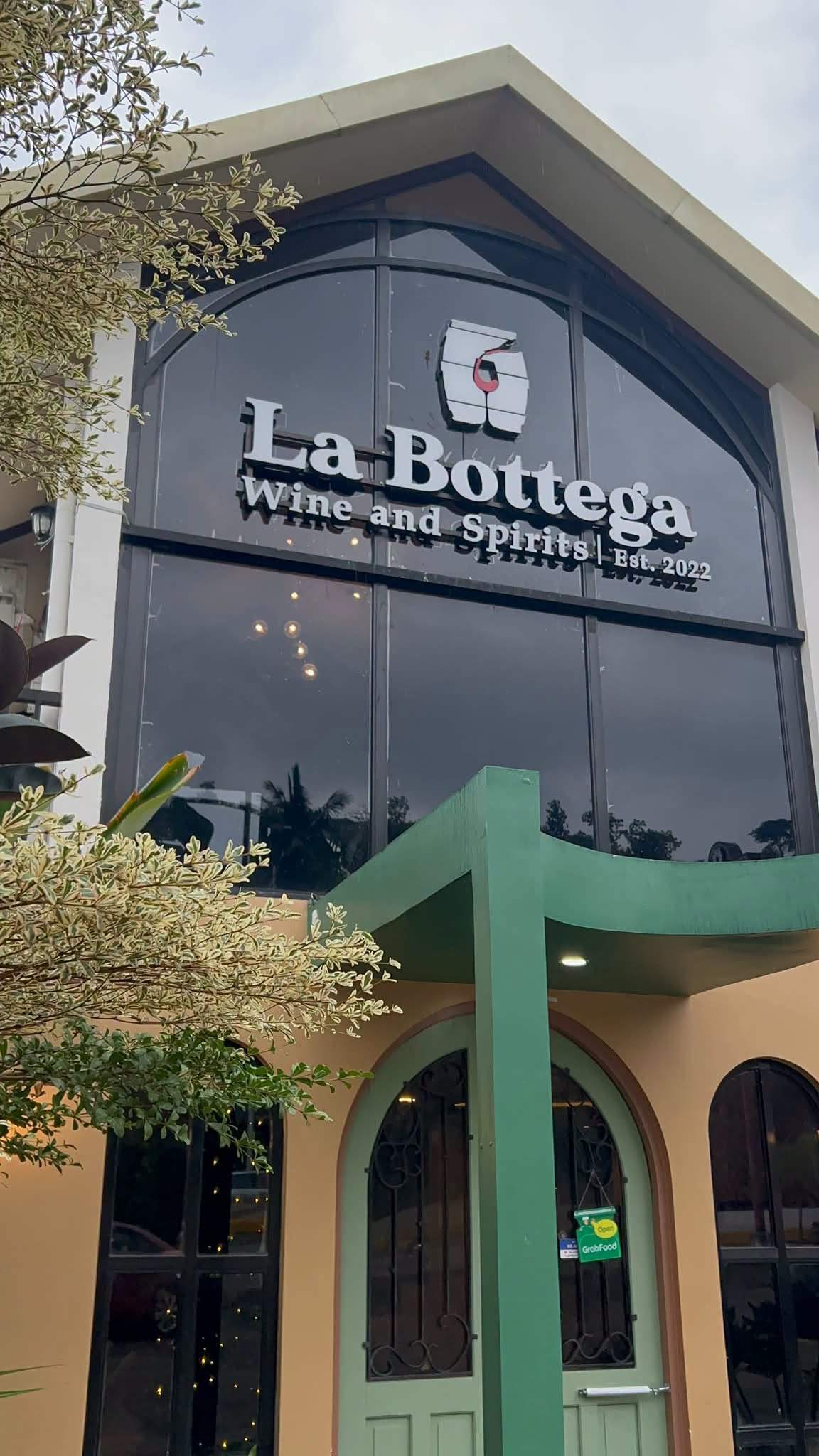 La Bottega Wine and Spirits signage above tall arched windows and a green canopy over the front door in Sambas