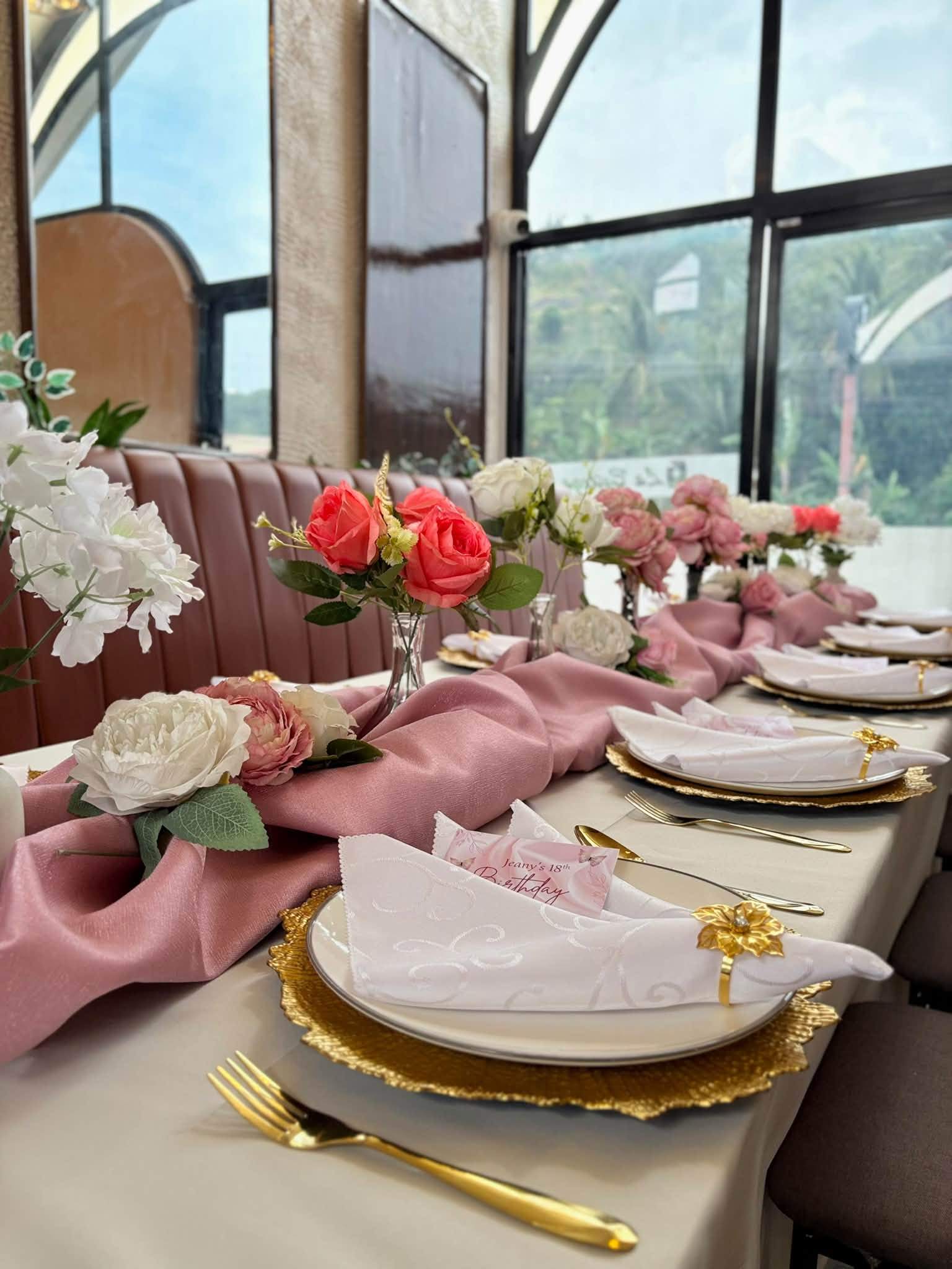 Pink table runner, roses and gold-rimmed plates beside large windows